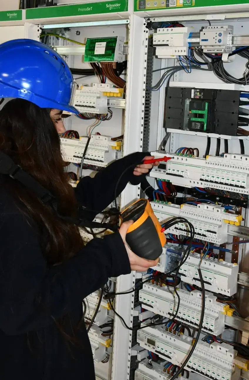 Technicienne CIDE effectuant un contrôle à la pince ampèremétrique sur une armoire électrique Schneider